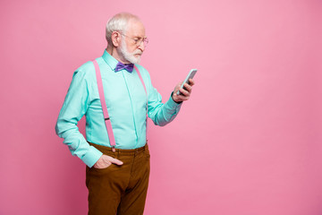 Profile side photo focused old man use smartphone check social network read repost share information frown face wear brown pants teal violet bow tie isolated pastel pink color background