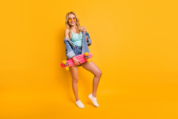 Fototapeta na wymiar Full body photo of attractive pretty lady long hairdo good mood hold pink skateboard weekend leisure wear casual teal singlet denim mini shorts shirt shoes isolated yellow color background