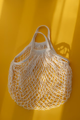 Fototapeta premium Empty mesh string bag on bright yellow background and hard sunshine. The concept of zero waste. Using reusable bags instead of disposable cellophane packets.