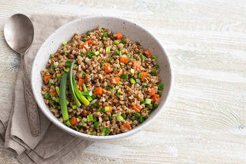 Delicious vegan buckwheat with vegetables and green onions on a light wooden background. Healthy homemade food