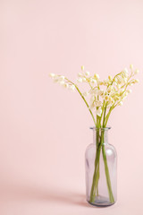 Greeting card with white lily of the valley on pink background for celebration Mothers Day, wedding, March 8. Nature concept. Home garden in vase. Summer green floral design. Selective focus.