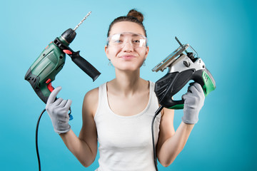 Young woman holds a jigsaw and a drill on a blue background