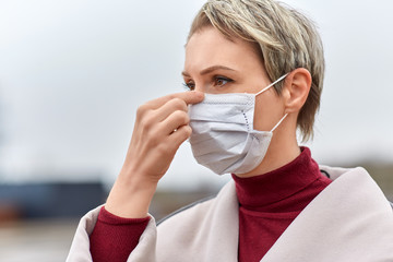 health, safety and pandemic concept - young woman wearing protective medical mask outdoors