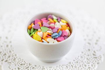 Candies in the form of multi-colored hearts lie in a white plate. Place for text.