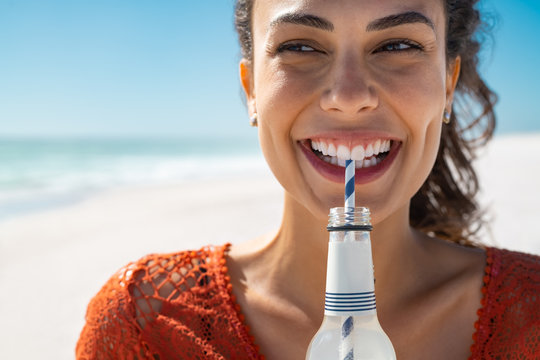 Young happy woman drinking soft drink on beach