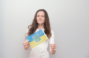 Young beautiful girl in embroidered shirt with Ukrainian flag. Attractive Ukrainian woman wearing traditional Ukrainian embroidery on the grey background.