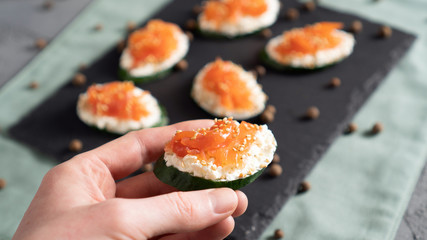 Concept of healthy sandwich alternative. Cucumber with cream cheese and salmon in the hand. Ready to eat.