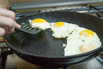 woman's hand using a black spatula takes a fried egg from the pan