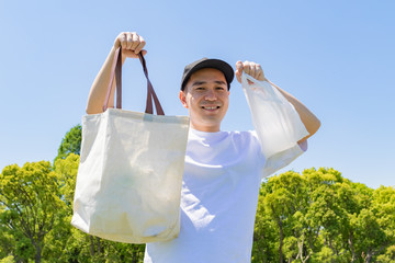 エコバックとレジ袋を持つ日本人男性。青空背景