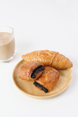 Chocolate and butter croissant on wooden plate with  glass of milk tea on white background                                                                   