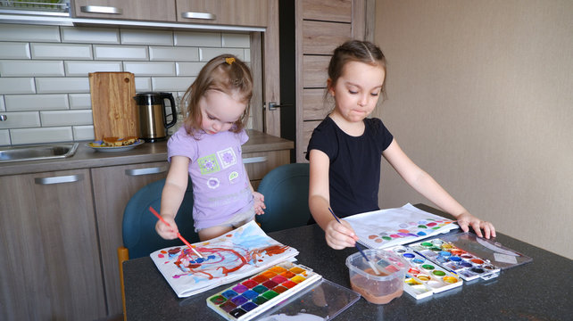 Two little girls sisters paint with children's paints at a table in the kitchen