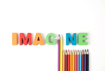  " IMAGINE " Multicolored Wooden Letters with Multicolored Pencil on White Background                                                            