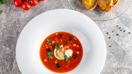 Ukrainian cuisine in European style. Solyanka soup with assorted sausages and meat. Beautiful serving dish in a restaurant in a white plate. background image, copy space text