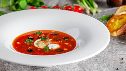 Ukrainian cuisine in European style. Solyanka soup with assorted sausages and meat. Beautiful serving dish in a restaurant in a white plate. background image, copy space text