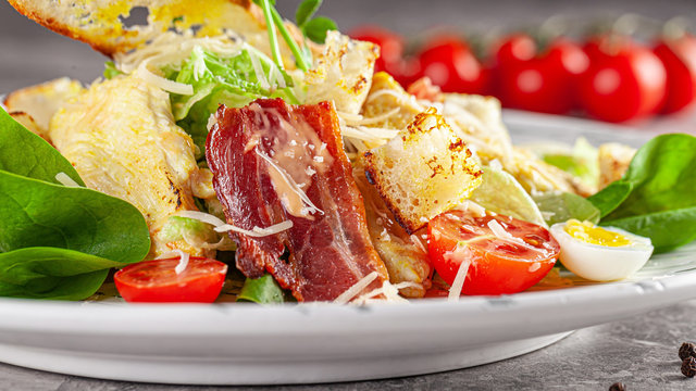 Italian Cuisine. Caesar salad with chicken, bacon, quail eggs, bread croutons, cherry tomatoes. Dish in a restaurant on a white plate. background image, copy space text