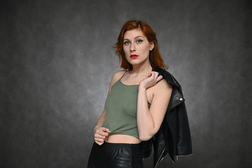 The model shows different emotions by changing poses. Portrait of a young pretty red-haired woman in a green T-shirt and a black jacket on a gray background.