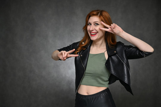 Portrait of a young pretty woman with beautiful hair and excellent make-up in a green T-shirt and a black jacket on a gray background. The model demonstrates vivid emotions by changing poses.