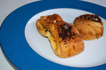.Two chocolate chips croissant on white and blue plate.A braid with chocolate .Swiss Brioche with Chocolate Chips (Brioches suisses). .