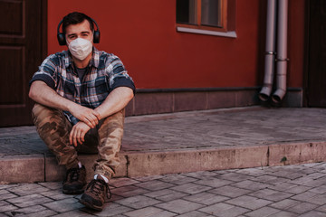 a guy in a mask and headphones sits on the doorstep home and listens to music