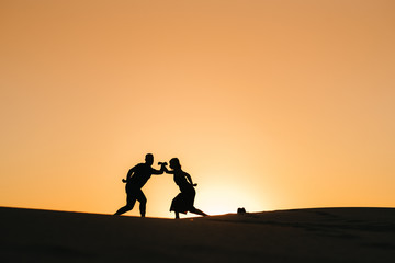 silhouettes of a happy young couple on a background of orange sunset in the sand desert