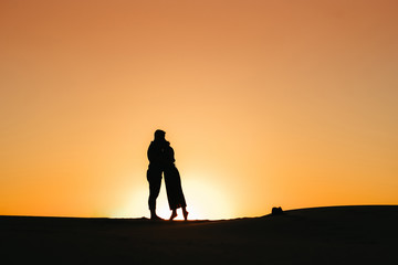 Fototapeta na wymiar silhouettes of a happy young couple on a background of orange sunset in the sand desert
