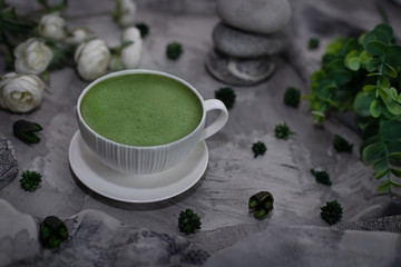 matcha green tea in a porcelain mug on a grey textured background with flowers and greenery
