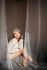 Obraz premium Beautiful girl with a mask for sits on the edge of the bed and smiles at the sun