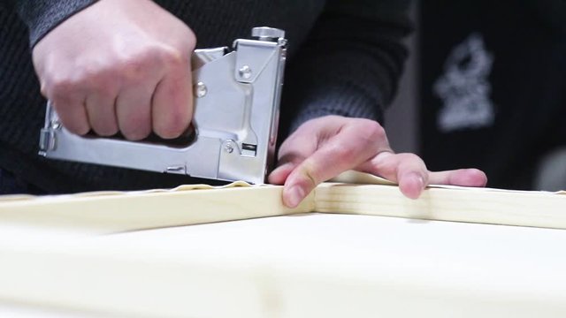 Canvas stretching. Wooden stretcher bar, staple gun, canvas pliers, male hands