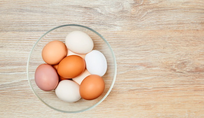 eggs of different colors from white to brown in a glass bowl on a wooden table surface