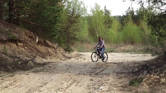 Young attractive woman rides a bicycle on a country road and looks around