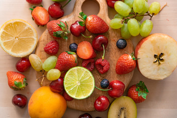 top view of mixed of summer fruit on wood table with natural light, strawberries, blueberries, lemon, lime, apple, kiwi, cherry, all fresh and ripe, base of healthy eating