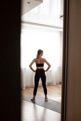 Beautiful girl at home in black sportswear is training on a black rug