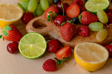 Fototapeta na wymiar mix of spring fruit on wooden table with natural light, strawberries, blueberries, lemon, lime, apple, kiwi, cherry, grape, all fresh and ripe, inviting and colorful,