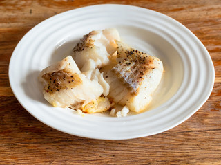 portion of baked and peppered cod fish on white plate on old wooden table in home kitchen