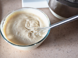 french whisk in glass bowl with freshly whipped Dalgona coffee (korean beverage made by whipping instant coffee powder, sugar and hot water) at home kitchen