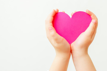 Closeup of child's hands holding paper pink heart on white background. Concept of love.