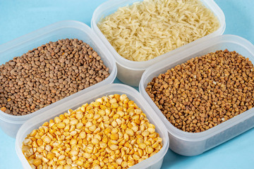 Raw rice, buckwheat and dry peas in plastic containers on blue background
