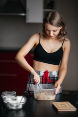 Beautiful girl in the kitchen mixes the ingredients in a plastic container
