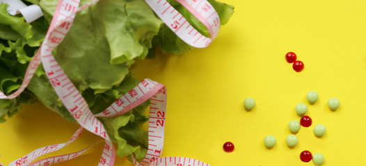 lettuce with measuring tape, pills of red and green color, lie on a yellow background. Weight loss, proper nutrition, vitamin C, K, A, seasonal vegetables, youth extract, weight loss after quarantine