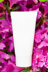 White tube with cream in pink azalea flowers close-up, concept of natural cosmetics