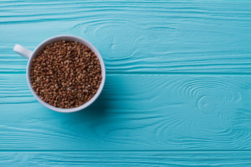 Cup of buckwheat grains top view. Copy space on blue wooden background.
