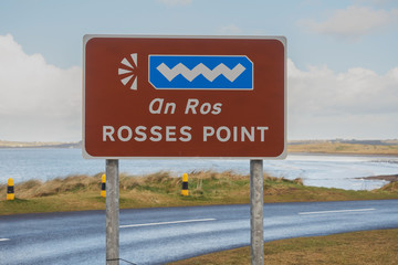 Rosses point sigh by the road. Ocean and cloudy sky in the background.
