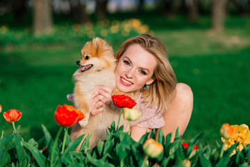 Attractive young woman holding dog spitz outside and smiling at camera, walking in the park.