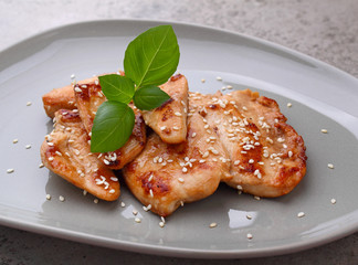 Fried chicken with soy sauce on a plate decorated with sesame seeds and basil