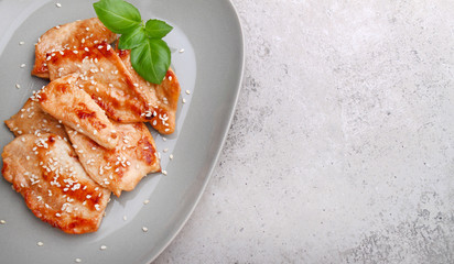 Fried chicken with soy sauce on a plate decorated with sesame seeds and basil, top view, copy space