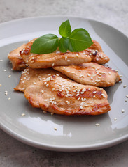 Fried chicken with soy sauce on a plate decorated with sesame seeds and basil.