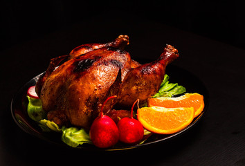 Baked Chicken with a crispy crust on a black background. With a substrate of lettuce leaves, orange slices and fresh radish. Just a shiny sour sweet chicken.