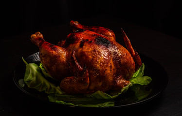 Baked Chicken with a crispy crust on a black background, with a substrate of lettuce leaves, orange slices. Just a shiny sour sweet chicken. Home cooking.