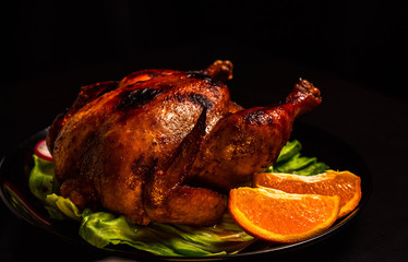 Baked Chicken with a crispy crust on a black background, with a substrate of lettuce leaves, orange slices. Just a shiny sour sweet chicken. Home cooking.