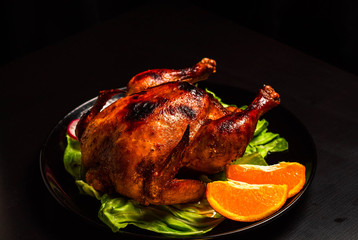 Baked Chicken with a crispy crust on a black background, with a substrate of lettuce leaves, orange slices. Just a shiny sour sweet chicken. Home cooking.